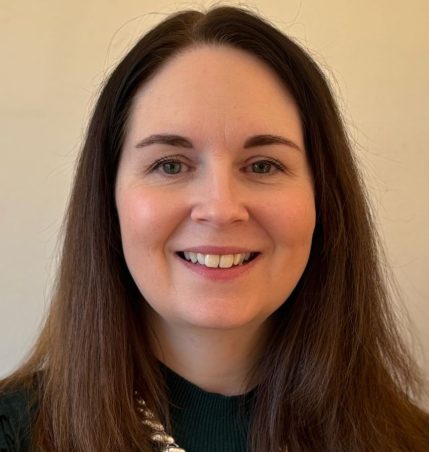 Mel wearing a dark green top, smiling at the camera.